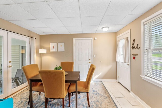 dining space with a healthy amount of sunlight, baseboards, a drop ceiling, and light tile patterned flooring