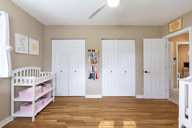 bedroom with two closets, baseboards, ceiling fan, and light wood-style flooring