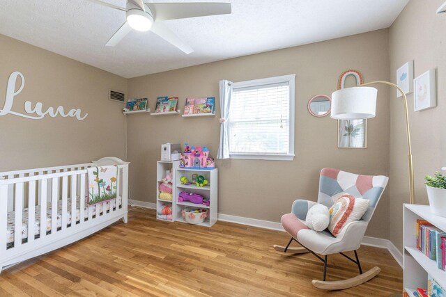 bedroom featuring ceiling fan, a crib, baseboards, wood finished floors, and visible vents