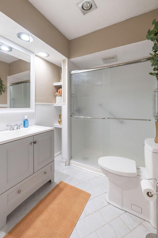 full bathroom featuring vanity, marble finish floor, toilet, a wainscoted wall, and a shower stall