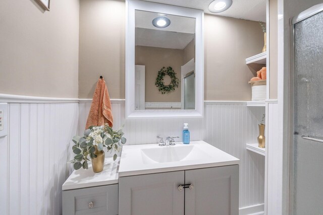bathroom featuring a wainscoted wall, a shower with door, and vanity