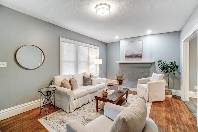 living area featuring baseboards, a textured ceiling, wood finished floors, and a fireplace