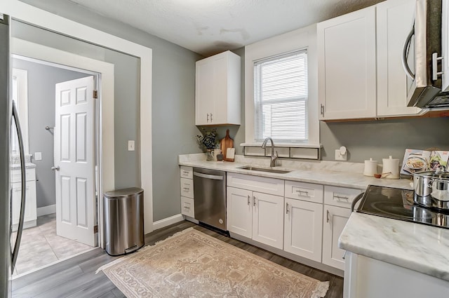 kitchen featuring appliances with stainless steel finishes, white cabinetry, a sink, light stone counters, and light wood-style flooring