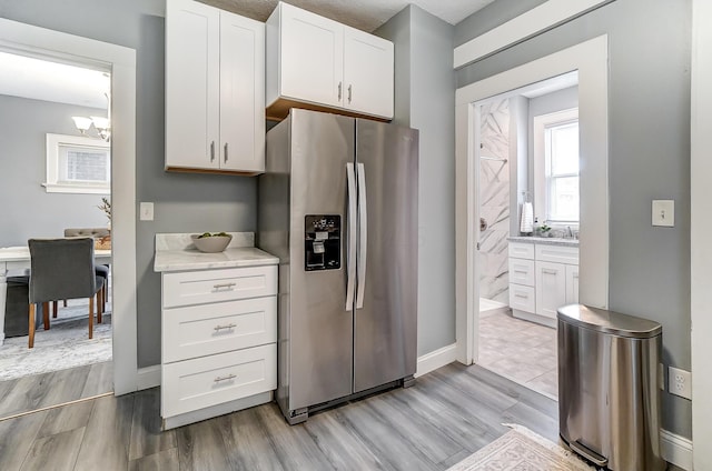 kitchen featuring stainless steel fridge, a chandelier, light wood-style flooring, white cabinetry, and baseboards