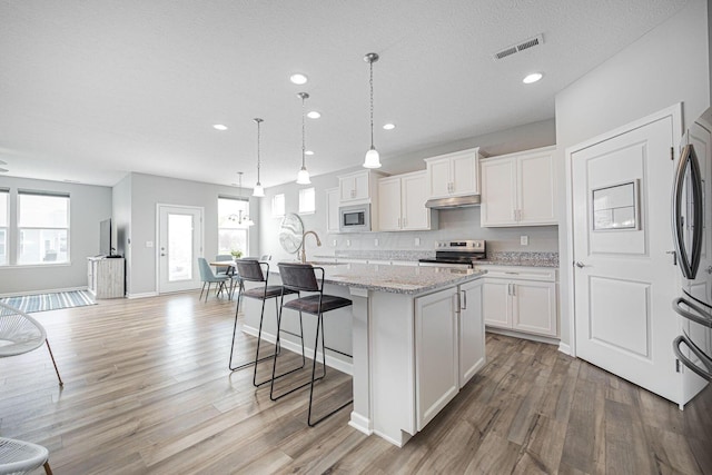 kitchen with a breakfast bar area, visible vents, appliances with stainless steel finishes, light wood-style flooring, and an island with sink