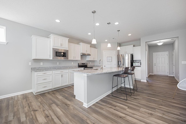kitchen featuring stainless steel appliances, white cabinetry, wood finished floors, and under cabinet range hood