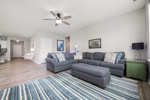 living room featuring a ceiling fan, baseboards, and wood finished floors