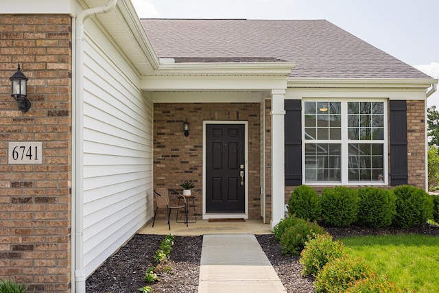 entrance to property featuring a shingled roof and brick siding