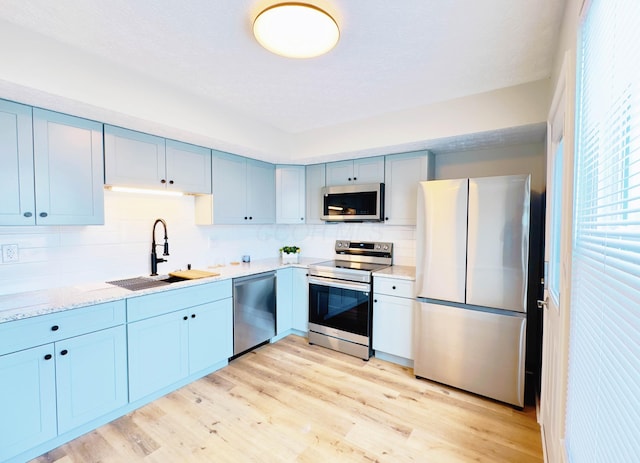 kitchen with a sink, blue cabinetry, stainless steel appliances, decorative backsplash, and light wood-type flooring