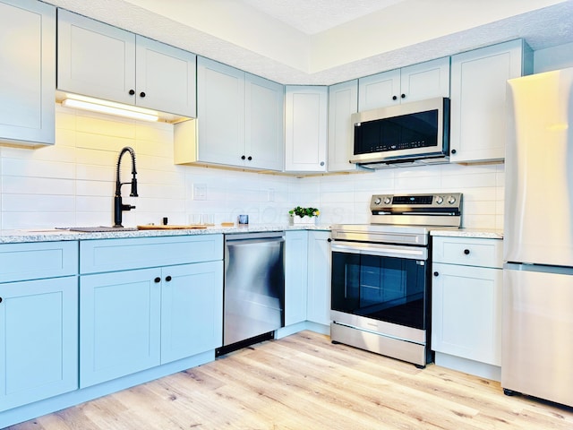 kitchen with a sink, light wood finished floors, appliances with stainless steel finishes, and tasteful backsplash