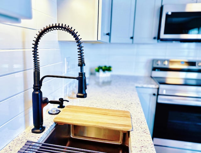 interior details with light stone counters, a sink, decorative backsplash, and appliances with stainless steel finishes