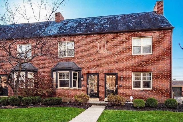 view of front of property featuring brick siding, a chimney, and a front lawn
