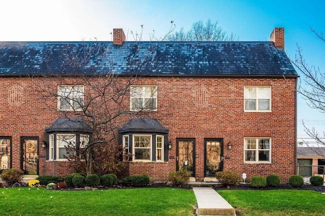 colonial home featuring brick siding, a chimney, and a front yard