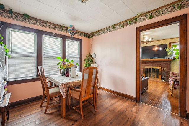 dining area with a brick fireplace, baseboards, a chandelier, and hardwood / wood-style floors