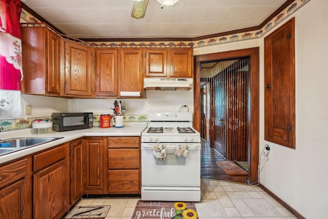 kitchen featuring white gas range oven, black microwave, light countertops, brown cabinetry, and under cabinet range hood