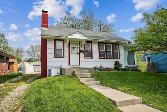 bungalow-style house featuring an outbuilding, driveway, a front yard, and a chimney