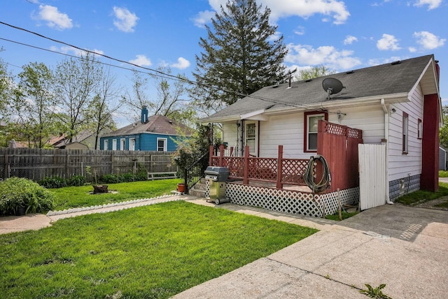 view of front of property with a deck, fence, a shingled roof, and a front yard