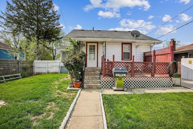 view of front of home featuring a fenced backyard, roof with shingles, a wooden deck, and a front lawn