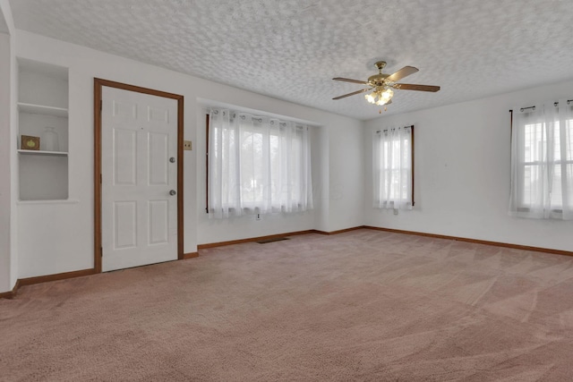 spare room with light colored carpet, a ceiling fan, a textured ceiling, and baseboards
