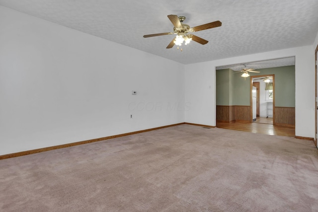carpeted empty room with a wainscoted wall, ceiling fan, and baseboards