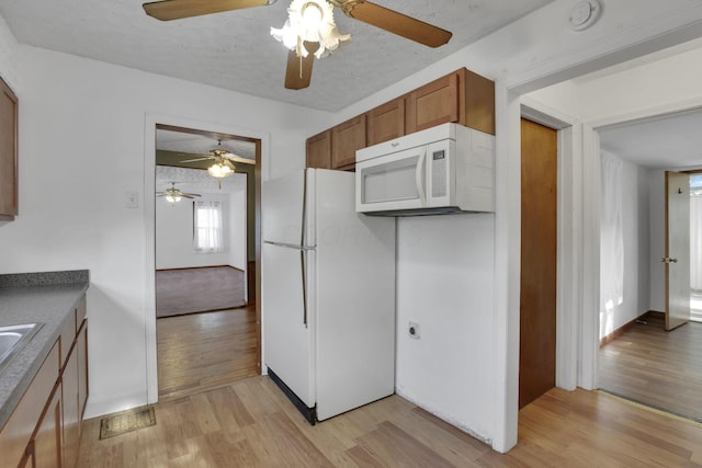 kitchen with ceiling fan, brown cabinets, baseboards, light wood-style floors, and white appliances