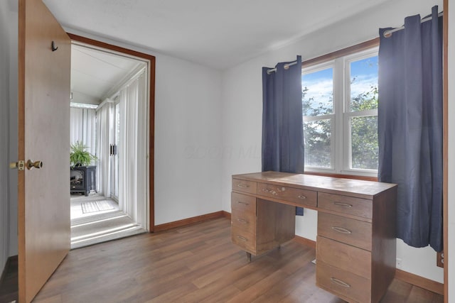 unfurnished office featuring vaulted ceiling, baseboards, a wood stove, and wood finished floors