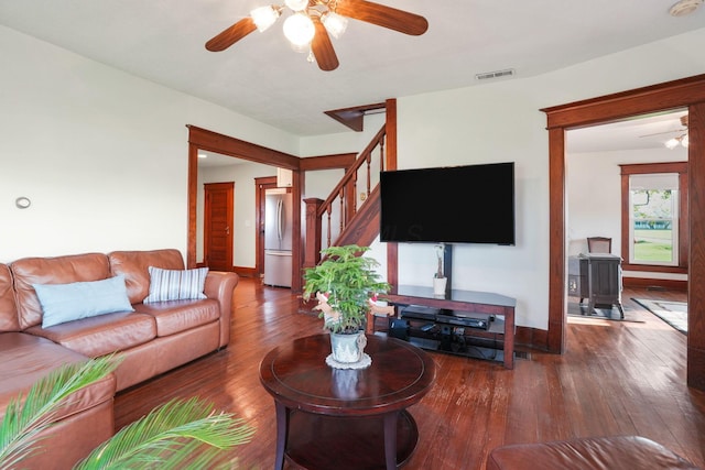 living room with stairway, ceiling fan, a wood stove, and hardwood / wood-style floors