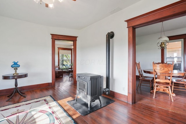 interior space featuring visible vents, a wood stove, wood finished floors, baseboards, and ceiling fan