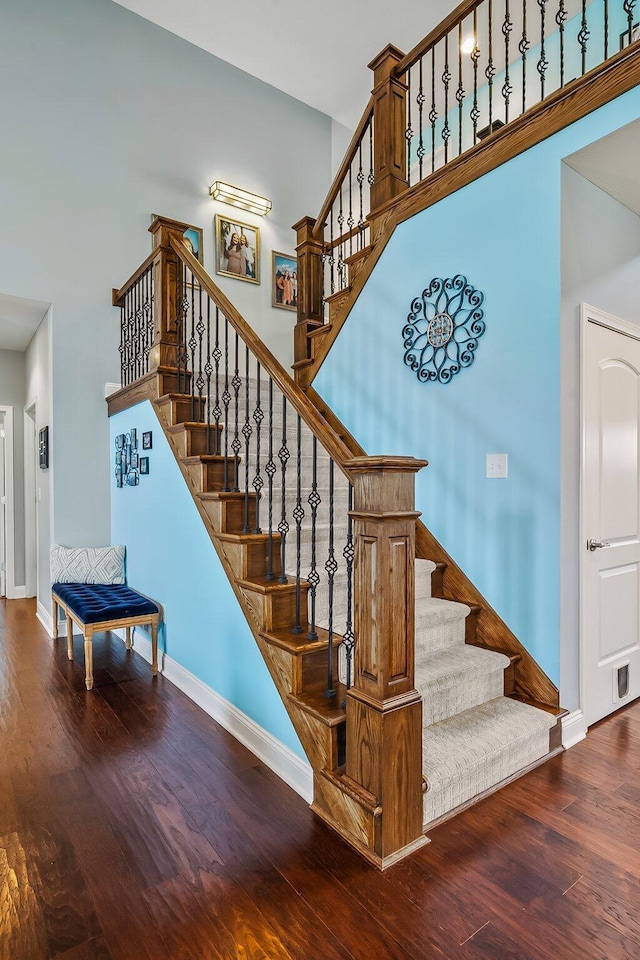 stairway featuring baseboards, a high ceiling, and wood finished floors
