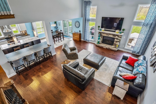 living room featuring a stone fireplace, baseboards, a high ceiling, and wood finished floors