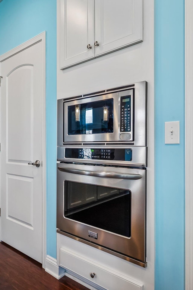 interior details featuring stainless steel appliances, white cabinetry, and dark wood-type flooring