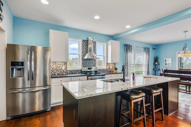 kitchen with wall chimney range hood, a sink, stainless steel appliances, decorative backsplash, and dark wood-style floors