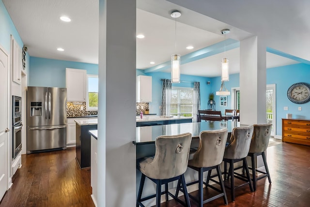 kitchen with white cabinets, a kitchen breakfast bar, stainless steel appliances, dark wood-type flooring, and backsplash