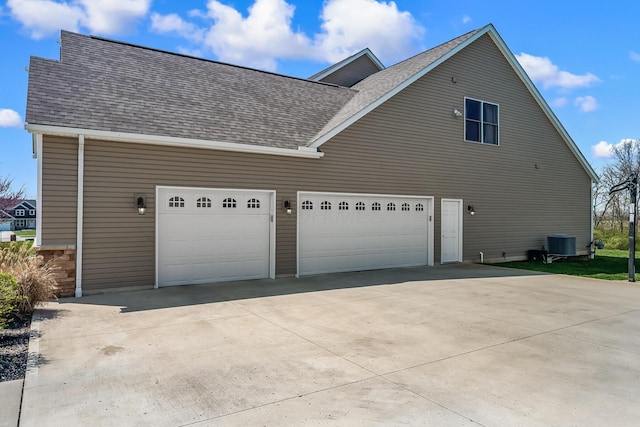 view of property exterior featuring an attached garage, a shingled roof, central AC, and concrete driveway