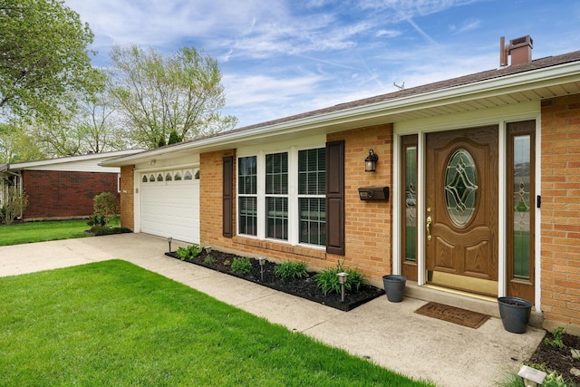 view of exterior entry featuring a chimney, brick siding, concrete driveway, an attached garage, and a yard