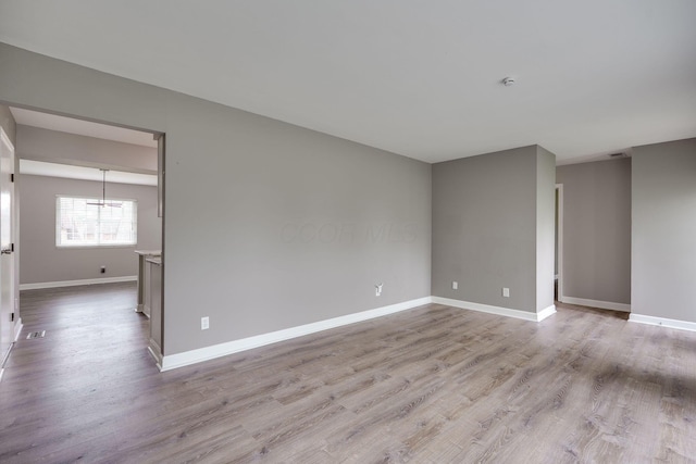 empty room featuring baseboards, wood finished floors, and a chandelier