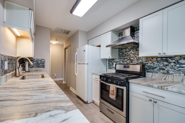 kitchen with visible vents, stainless steel gas stove, wall chimney range hood, a sink, and backsplash