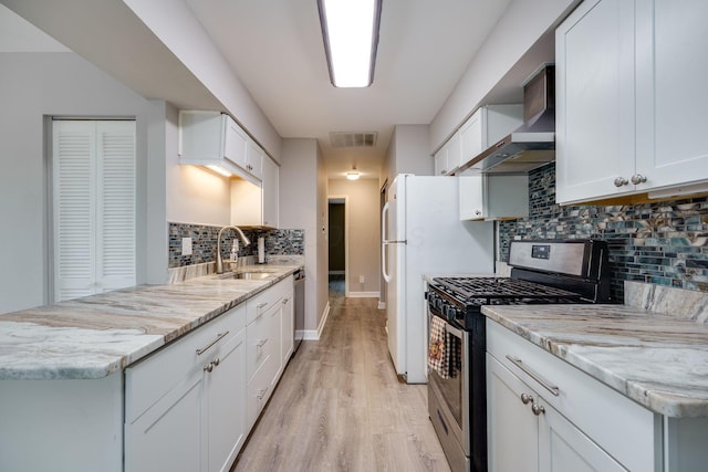kitchen featuring decorative backsplash, light wood-type flooring, a sink, stainless steel appliances, and wall chimney exhaust hood