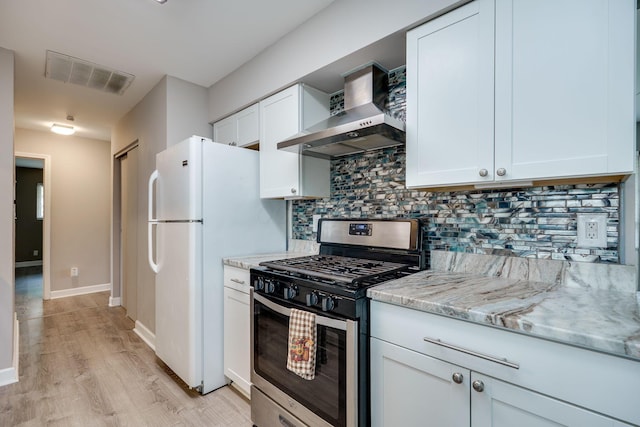 kitchen featuring wall chimney range hood, visible vents, tasteful backsplash, stainless steel range with gas cooktop, and light wood-style floors