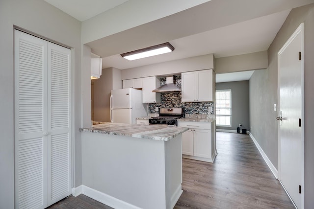 kitchen with freestanding refrigerator, decorative backsplash, wall chimney range hood, white cabinetry, and gas stove