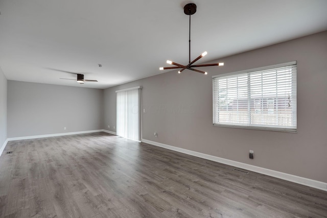 empty room featuring baseboards, ceiling fan with notable chandelier, wood finished floors, and visible vents