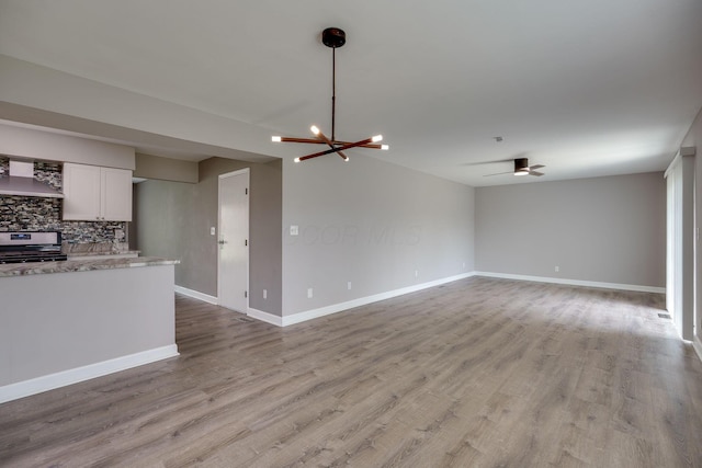 unfurnished living room featuring baseboards, light wood-style flooring, and ceiling fan with notable chandelier