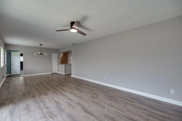unfurnished living room featuring baseboards, ceiling fan with notable chandelier, and wood finished floors