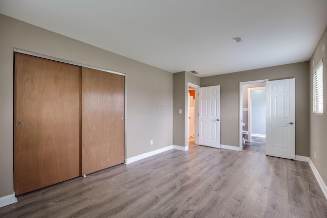 unfurnished bedroom featuring baseboards, a closet, wood finished floors, and visible vents