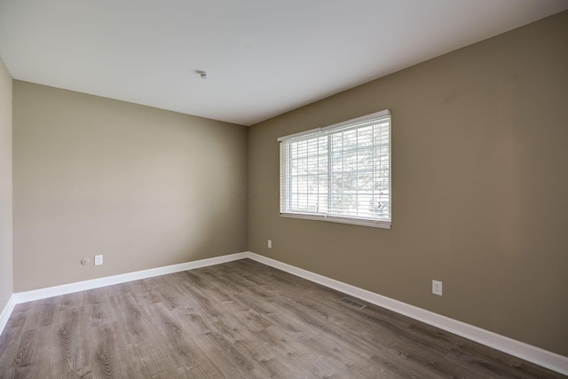 empty room with baseboards, visible vents, and wood finished floors