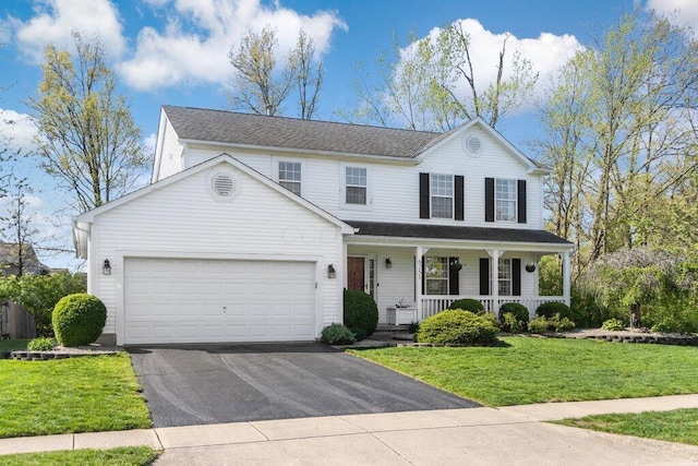 traditional home featuring covered porch, an attached garage, a front yard, and aphalt driveway