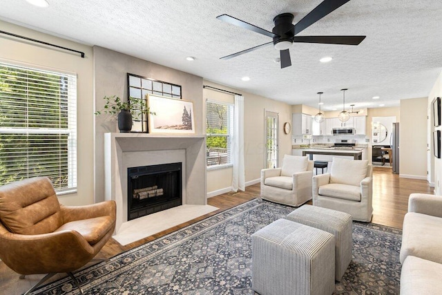 living area with a ceiling fan, a textured ceiling, a fireplace with flush hearth, and wood finished floors