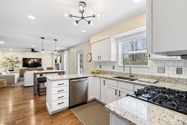 kitchen with a sink, dishwasher, a textured ceiling, a peninsula, and open floor plan