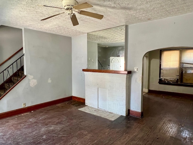 unfurnished living room featuring a ceiling fan, a textured ceiling, baseboards, and stairway