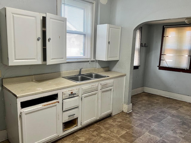 kitchen with light countertops, white cabinetry, baseboards, and a sink